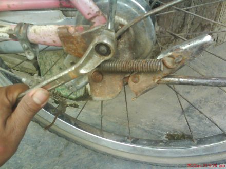 melepas mur pada as roda belakang dengan kunci pas/ring ukuran 14